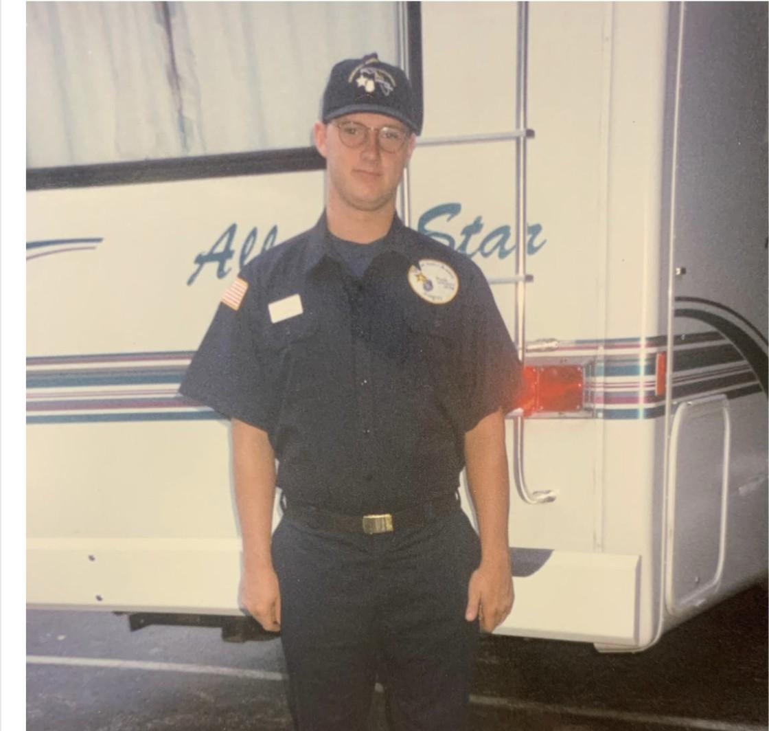 A young Wayne Partello in a police academy uniform standing in front of an RV.