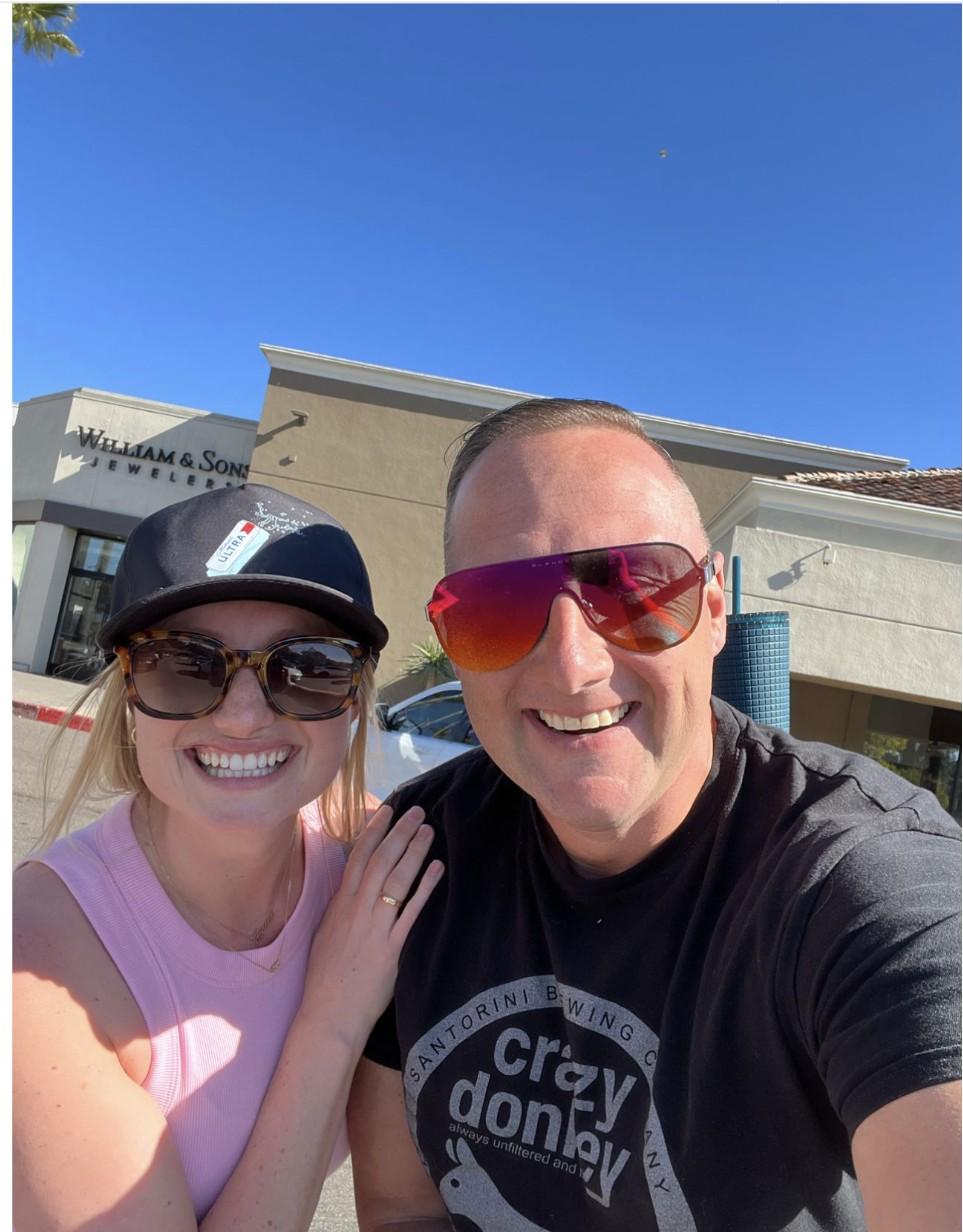 Wayne Partello smiling in a selfie with former mentee Allyson Sinkevich (Reilly) outside a shopping center under a clear blue sky.