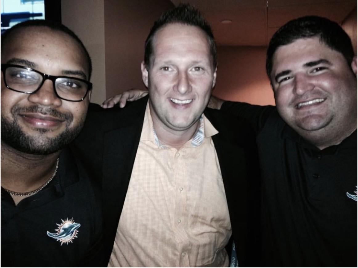 Wayne Partello poses with two Miami Dolphins colleagues wearing Dolphins-branded polos.