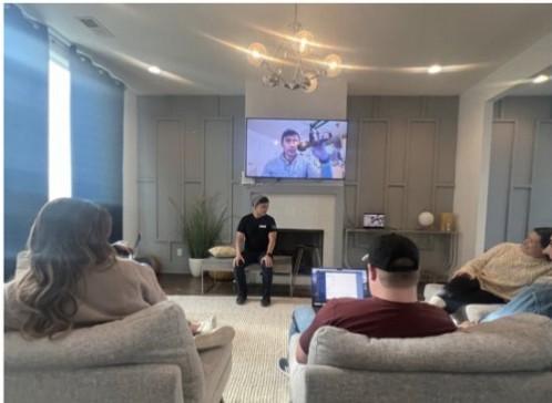The CUENTO team gathered in a living room watching a presentation on a wall-mounted screen.
