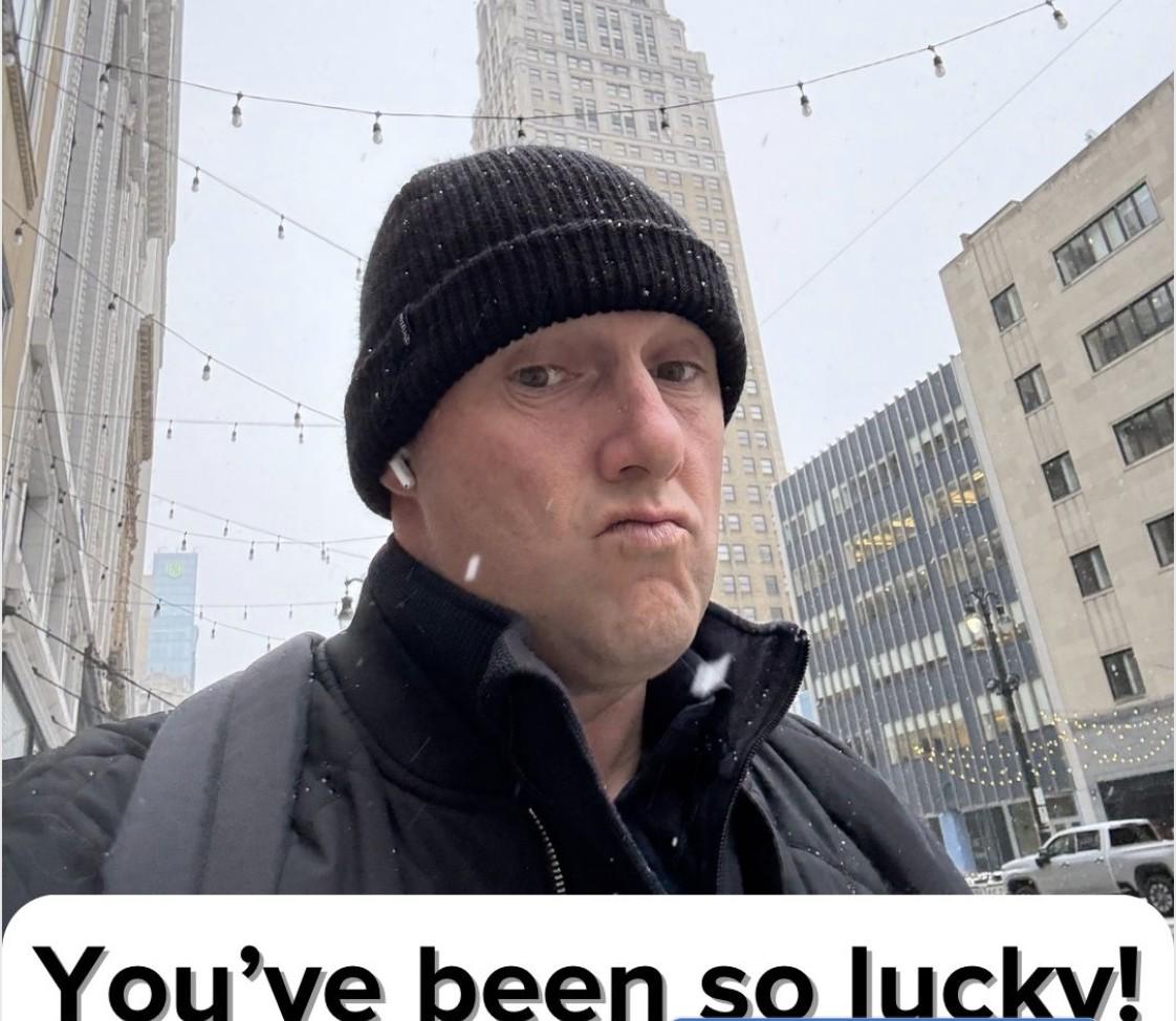 Wayne Partello selfie on a snowy city street wearing a beanie, with bold text overlay reading 'You've been so lucky!'