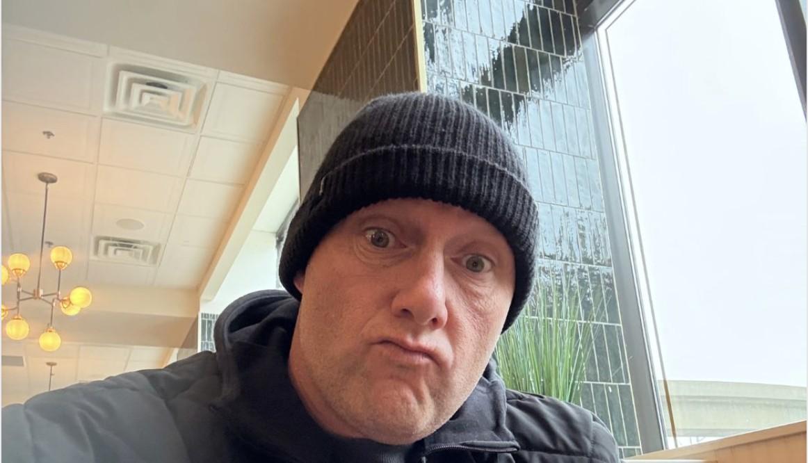 Playful close-up selfie of Wayne Partello wearing a dark beanie and jacket, making a skeptical expression