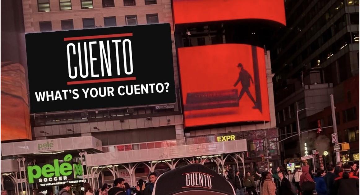 CUENTO's 'What's Your CUENTO?' advertising billboard lit up in Times Square, New York City, with Wayne Partello wearing a CUENTO cap in the foreground