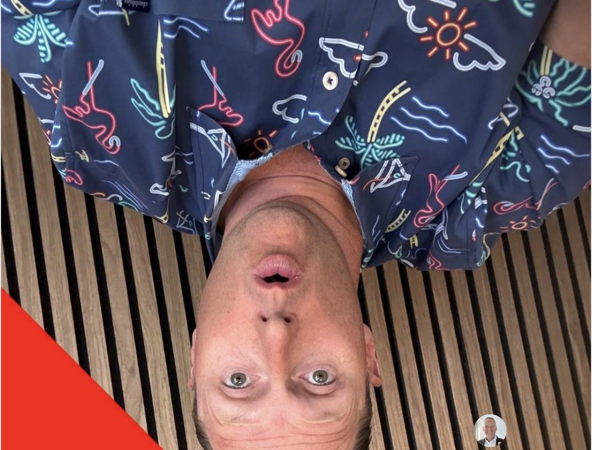 Wayne Partello taking a playful upside-down selfie on a wooden deck