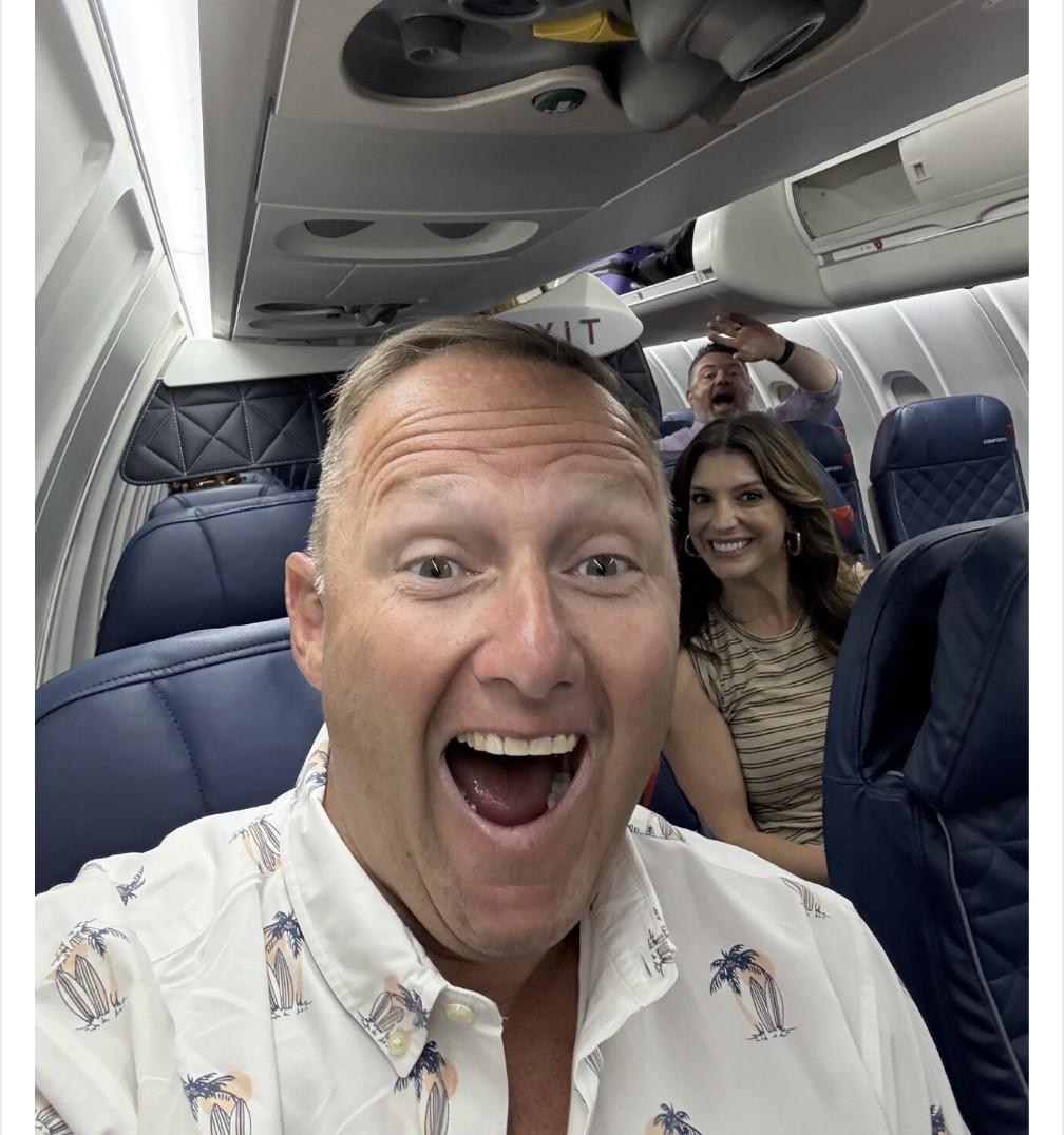 Wayne Partello taking an excited selfie on an airplane with two CUENTO team members laughing behind him