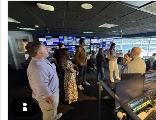 A group touring a stadium broadcast control room filled with monitors and production equipment