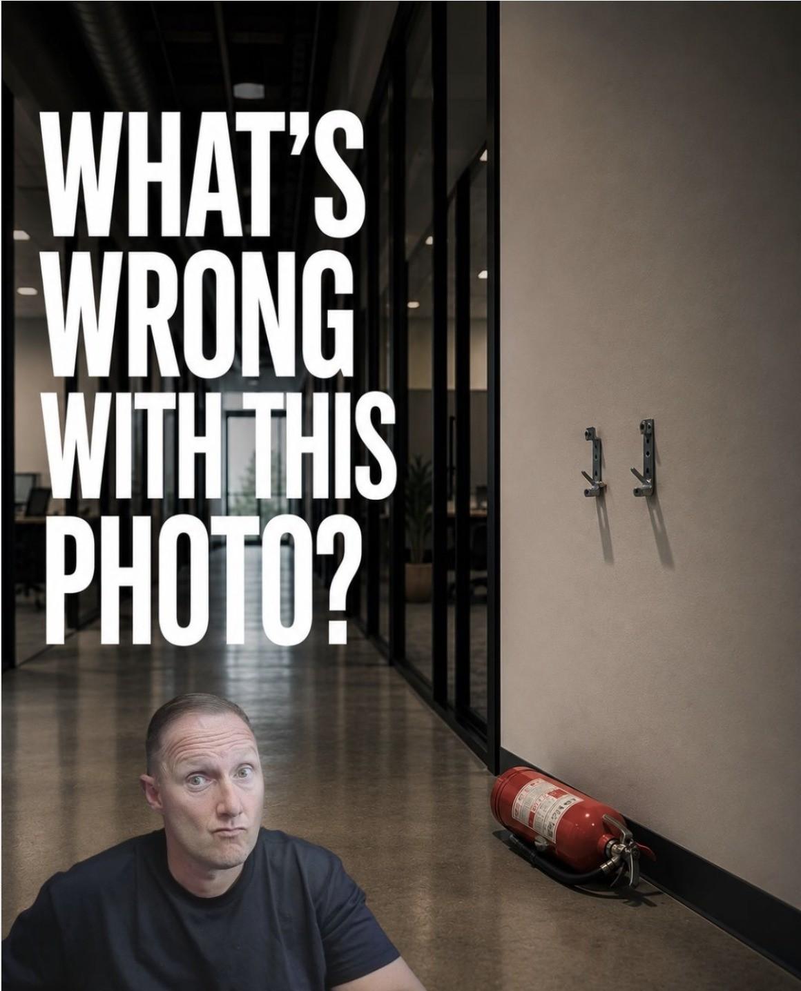"What's Wrong With This Photo?" graphic with Wayne Partello sitting in an office hallway next to a fire extinguisher that has fallen off its wall bracket.